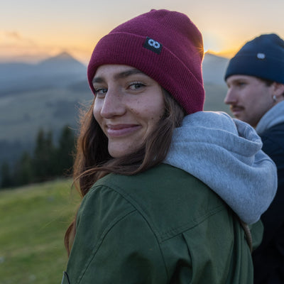 Photographer wearing a berry beanie with cooph logo and field jacket in a mountainous landscape. 