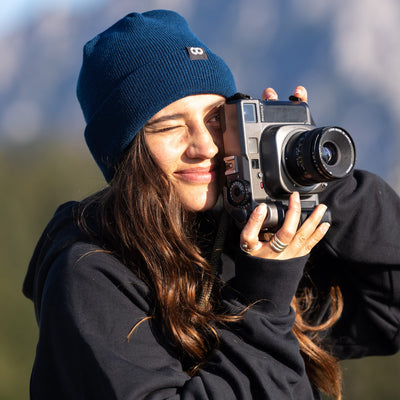 Photographer with vintage camera wearing the cooph edc beanie with a blurred natural background 