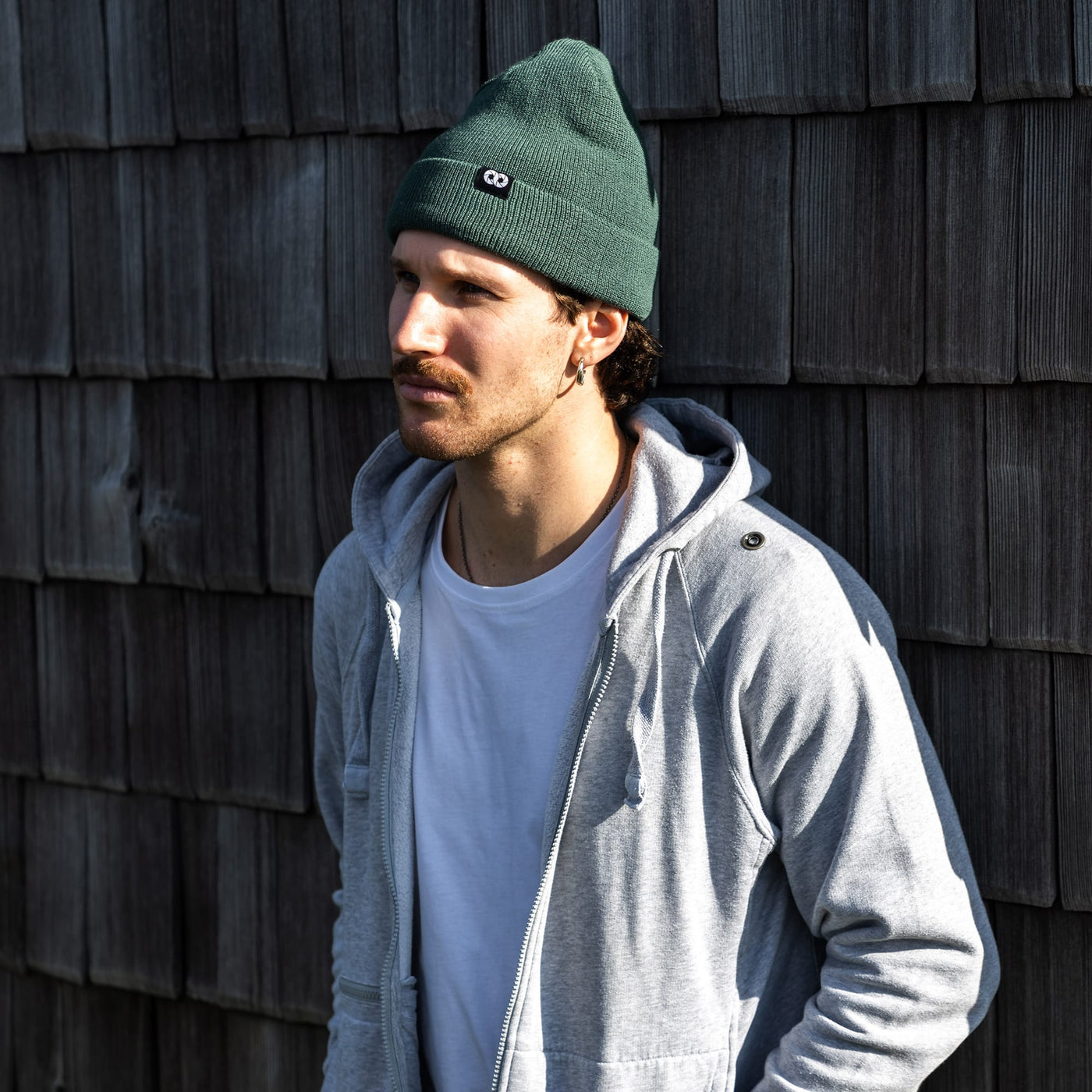 Photographer wearing a moss edc beanie and gray jacket against a wooden wall 