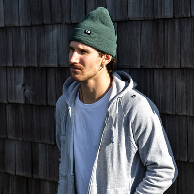 Photographer wearing a moss edc beanie and gray jacket against a wooden wall 
