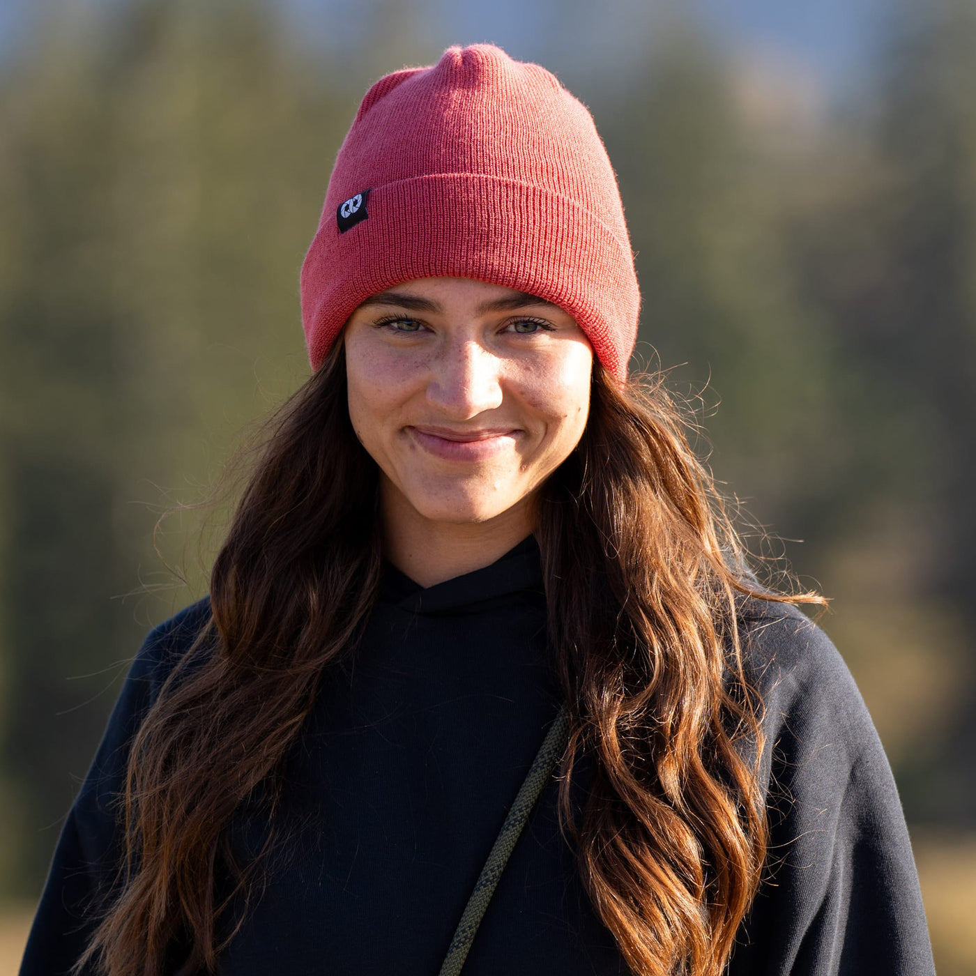 Photographer wearing a salmon edc beanie and black jacket outdoors with a blurred natural background 
