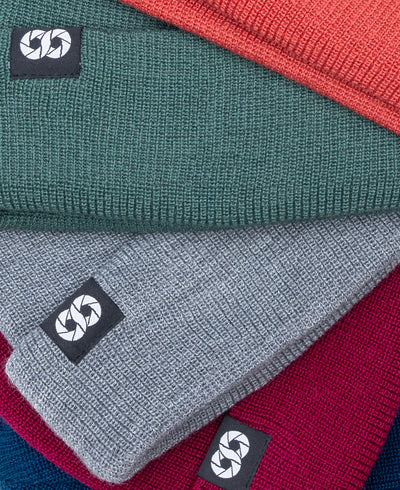 Stack of folded beanies in red, green, gray, and blue with a brand logo on a white background.