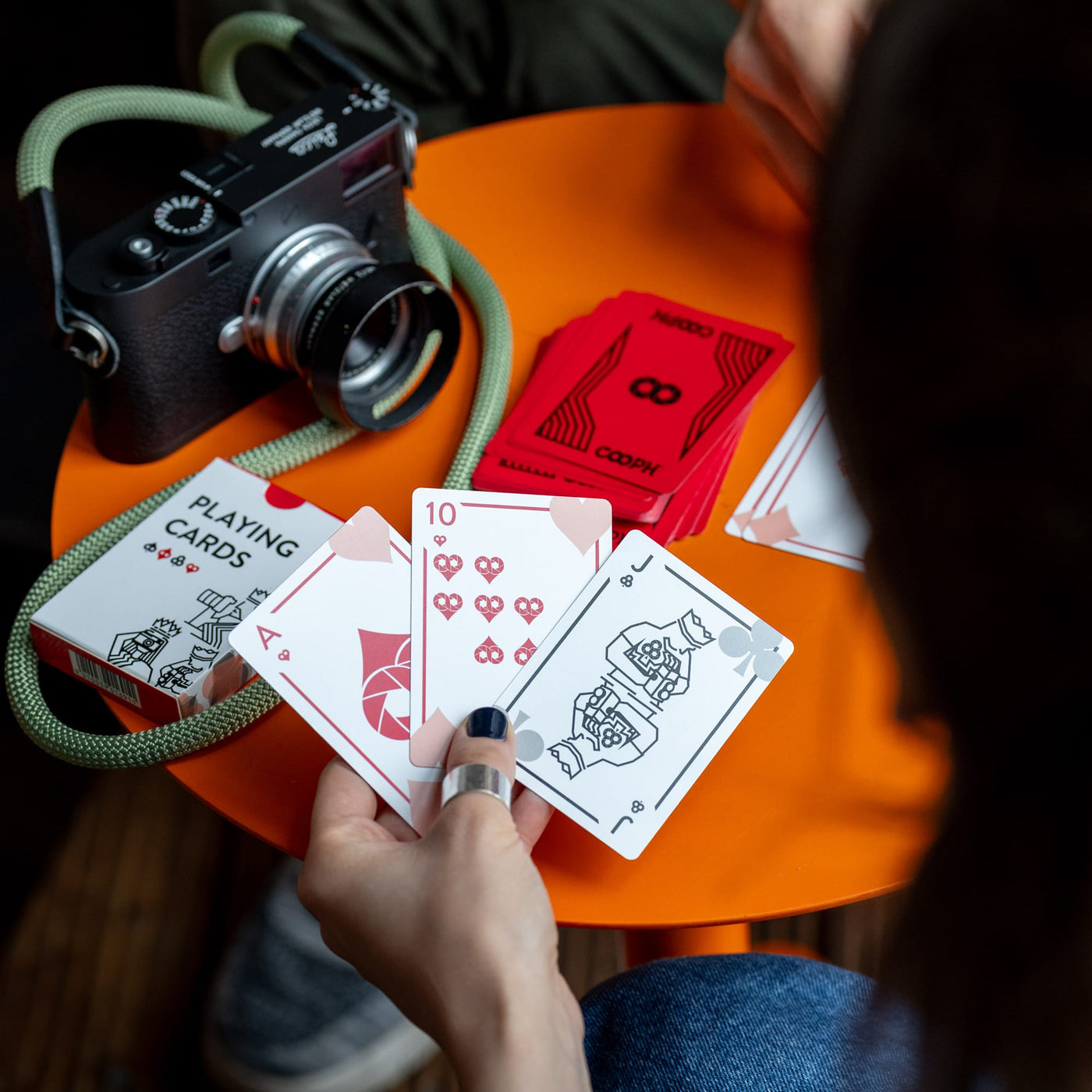 Person holding cooph playing cards next to a camera on an orange table 