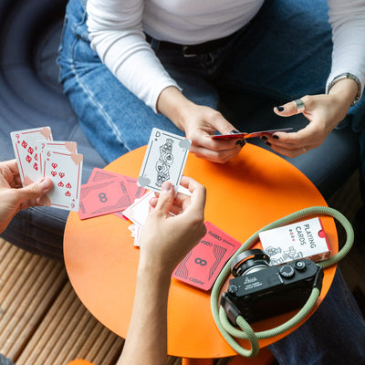 People playing cards on an orange table with a camera and strap in the foreground. 