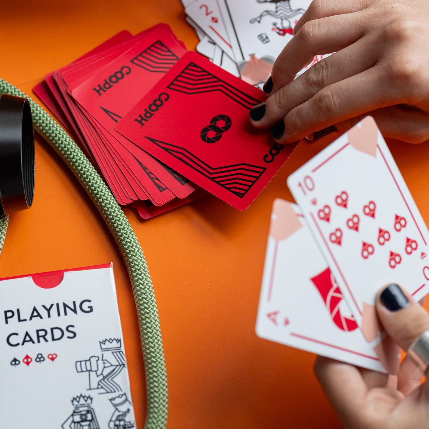 Original Cooph playing cards on an orange surface with hands holding cards 