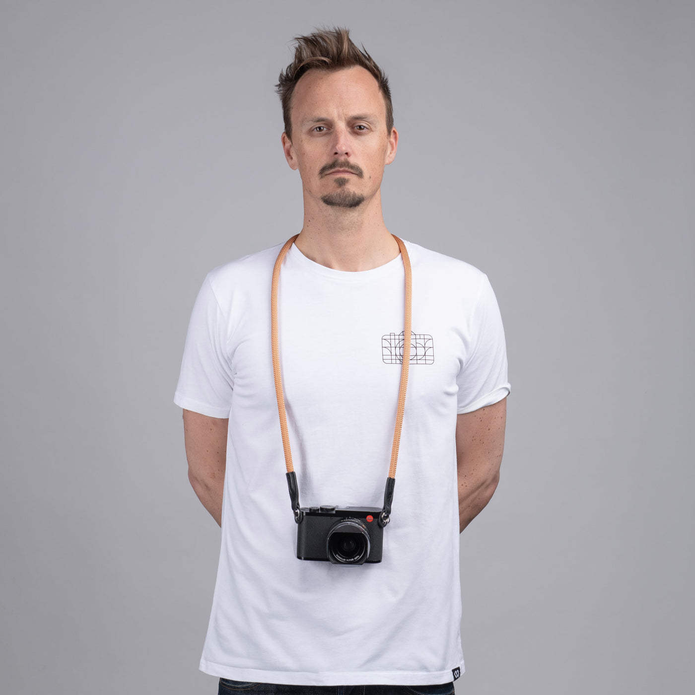 Photographer in a white t-shirt wearing a Leica camera around his neck with a Peach rope strap 