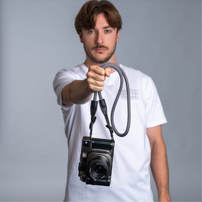 Photographer holding a camera with the cooph rope camera strap against a plain background 