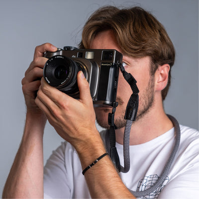 Photographer holding a vintage camera in his hands and the cooph rope camera strap arround his neck 