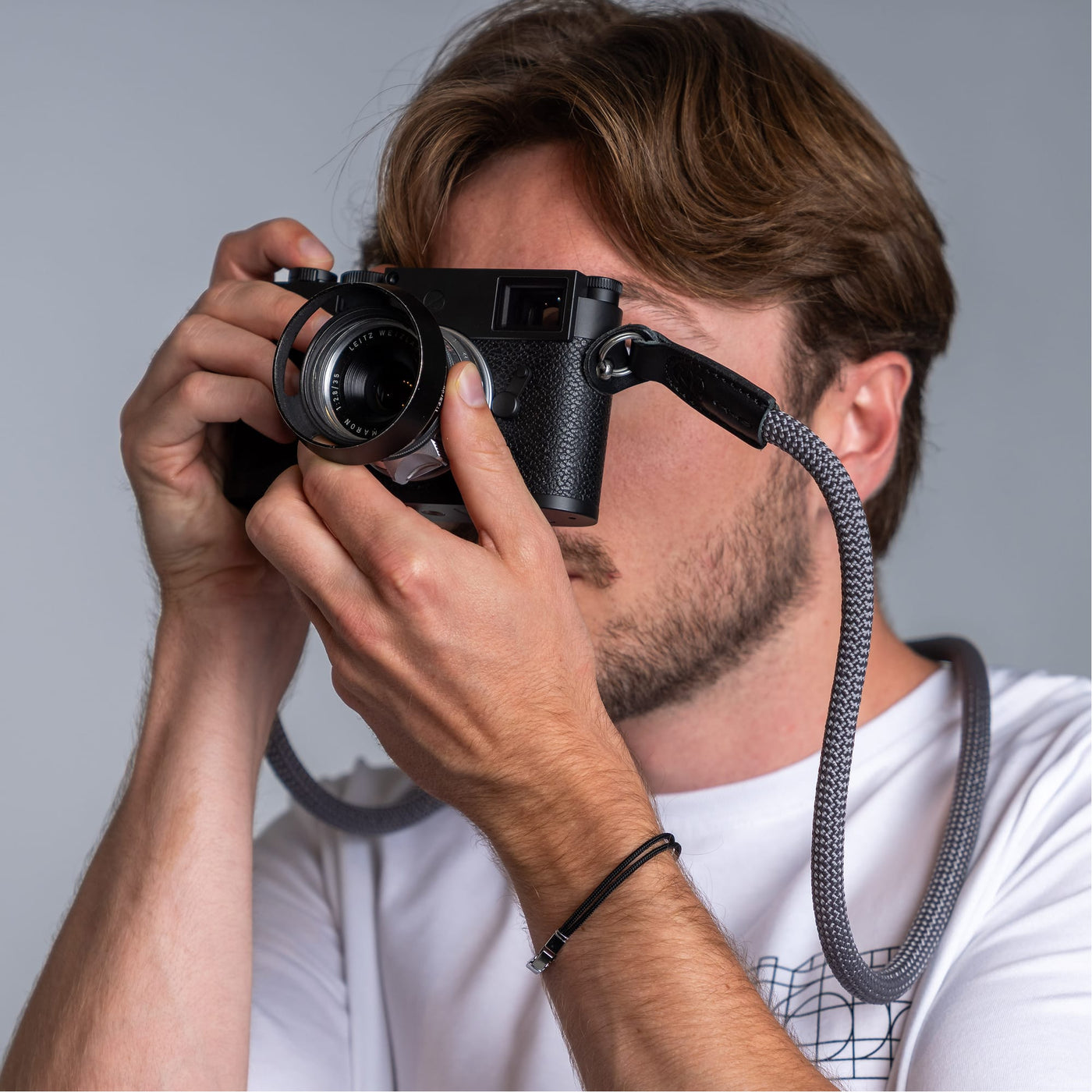 Photographer holding a leica camera in his hands and the cooph rope camera strap arround his neck 