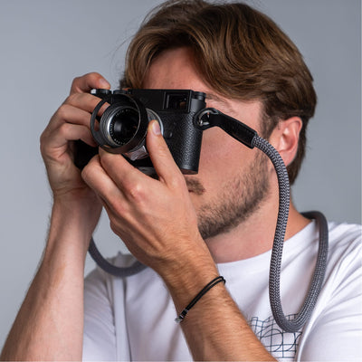 Photographer holding a leica camera in his hands and the cooph rope camera strap arround his neck 