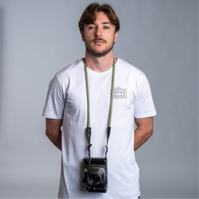 Photographer holding a camera with the cooph rope camera strap against a plain background  