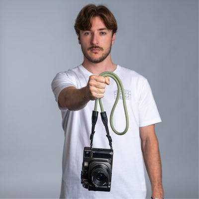 Photographer holding a camera with the cooph rope camera strap against a plain background 