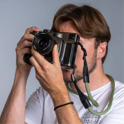 Photographer holding a vintage camera in his hands and the cooph rope camera strap arround his neck 