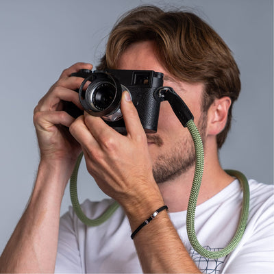 Photographer holding a leica camera in his hands and the cooph rope camera strap arround his neck 