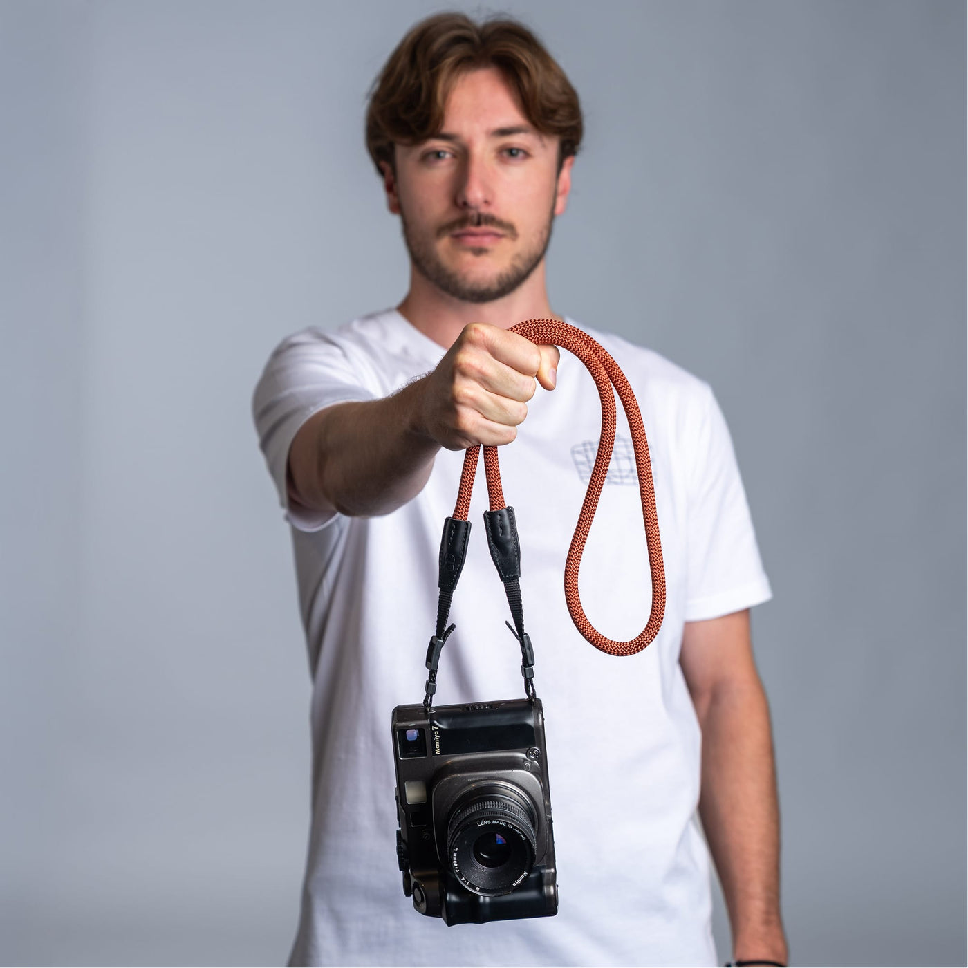 Photographer holding a camera with the cooph rope camera strap against a plain background 