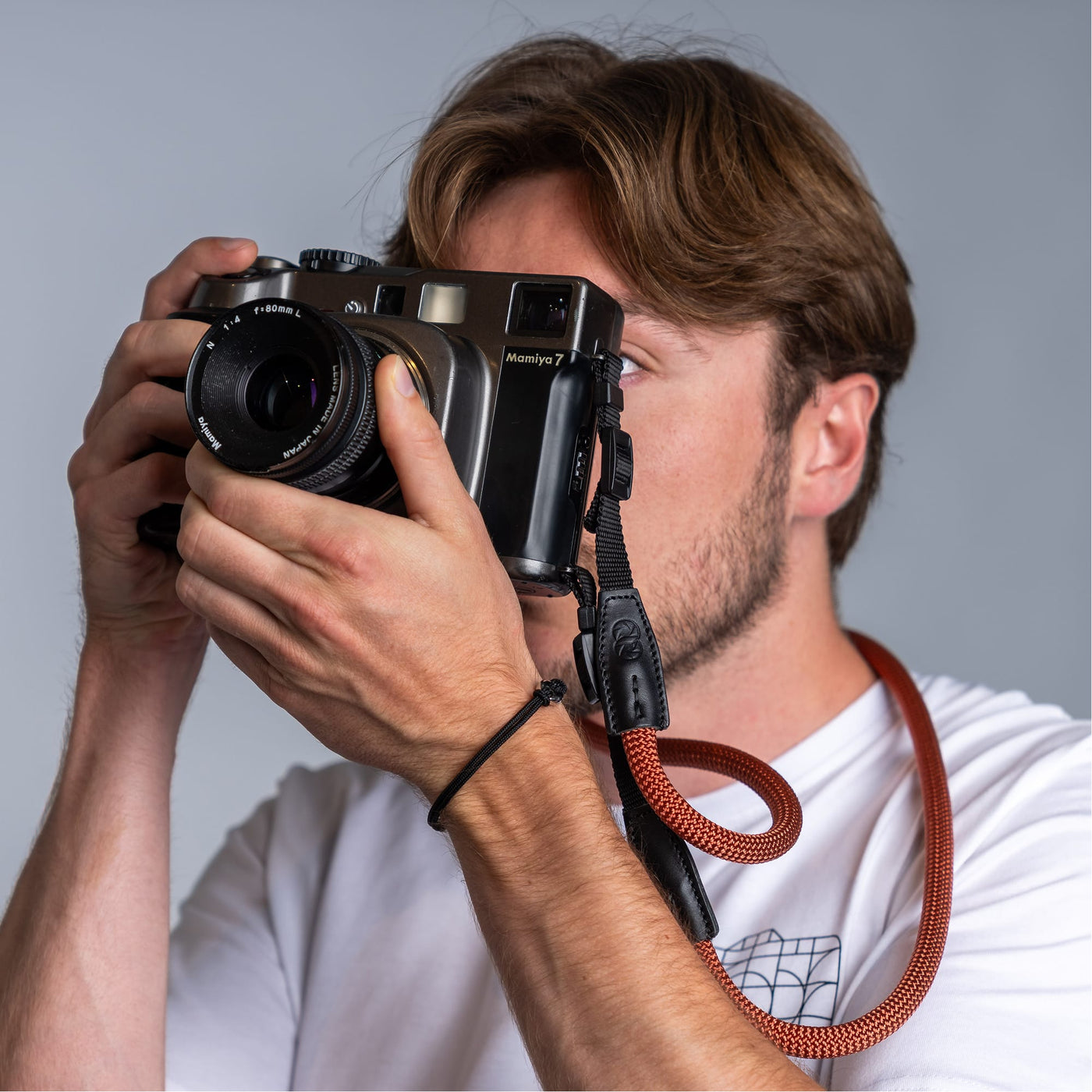 Photographer holding a vintage camera in his hands and the cooph rope camera strap arround his neck .