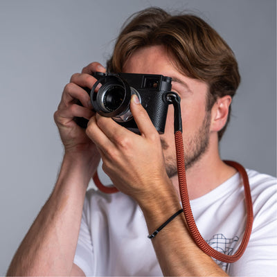 Photographer holding a leica camera in his hands and the cooph rope camera strap arround his neck . 