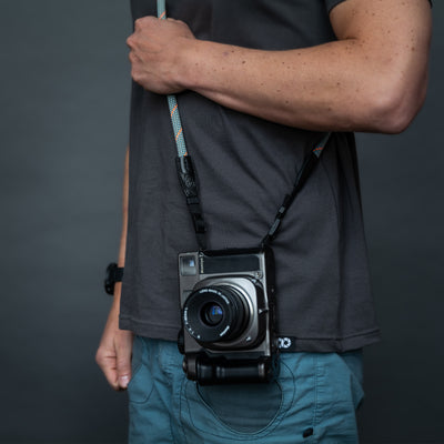 Camera on a photographer's hip held with gray rope strap 